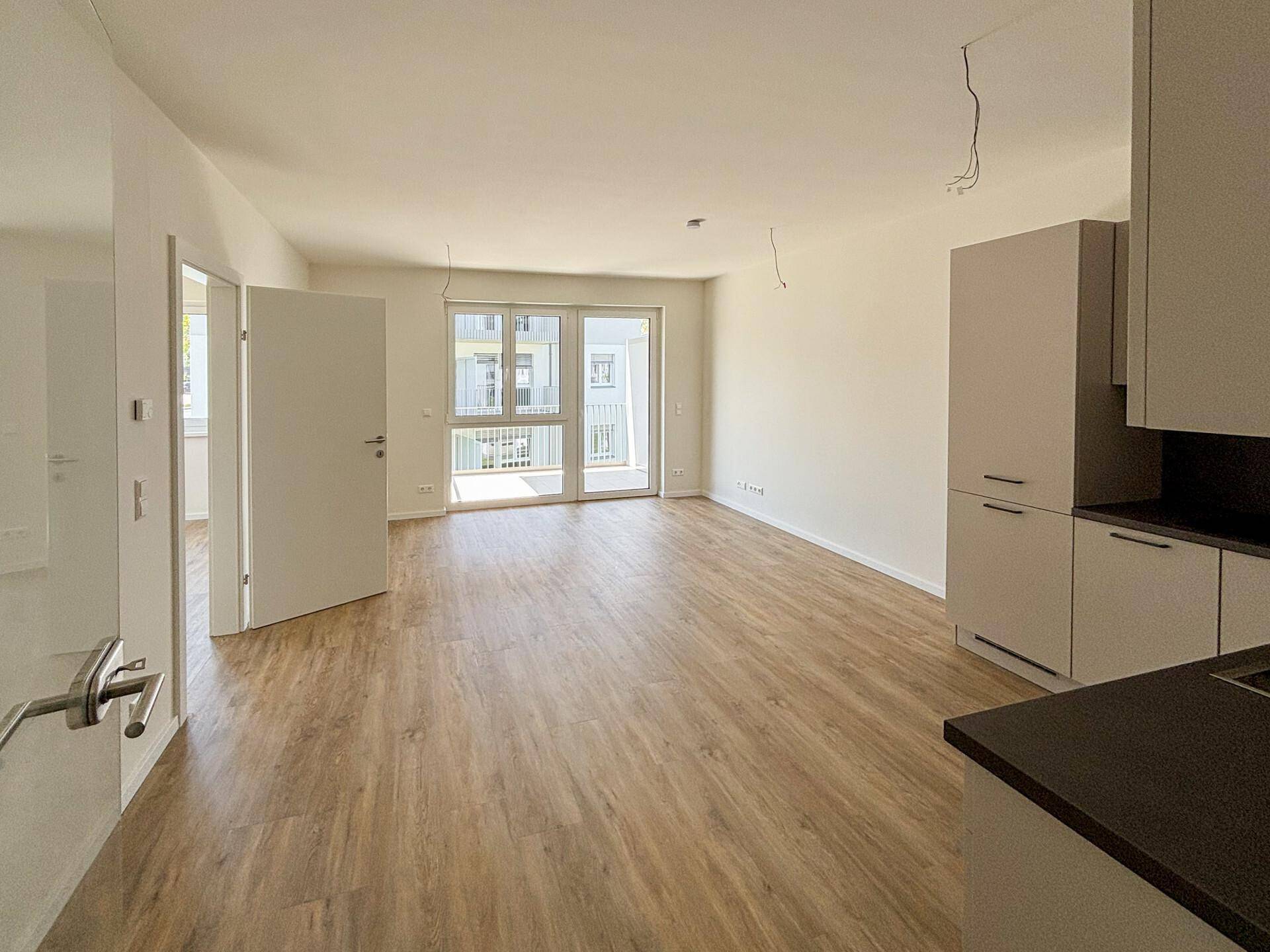 Geräumiger, heller Wohnbereich mit Laminatboden und Zugang zum Balkon.