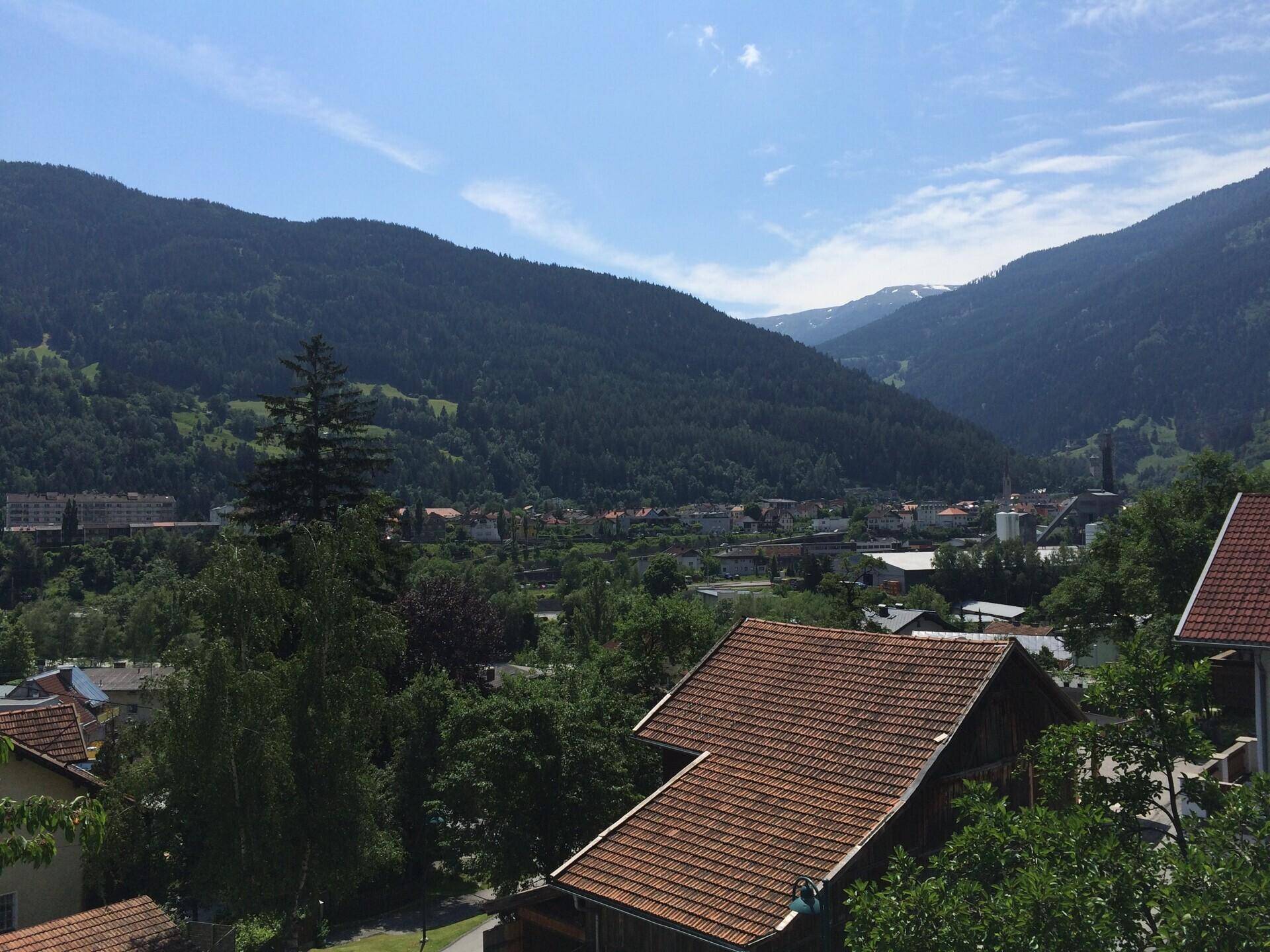 Panoramablick über ein Tal mit Häusern, Wäldern und majestätischen Bergen im Hintergrund.