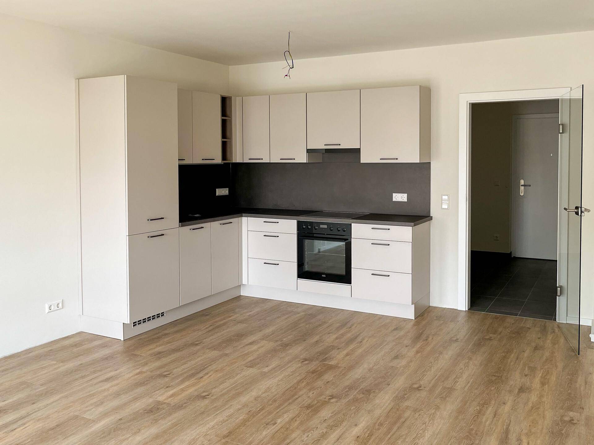 Neue Einbauküche mit hellen Schränken, dunkler Arbeitsplatte und integriertem Backofen.
