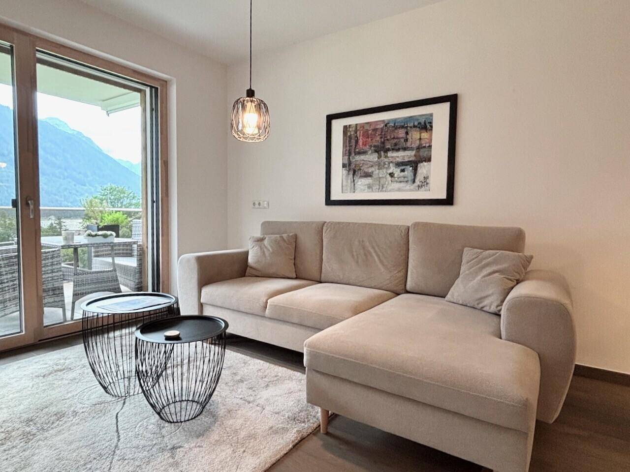 Helles Wohnzimmer mit beigem Sofa, modernen Beistelltischen und Zugang zur Terrasse mit Bergblick.
