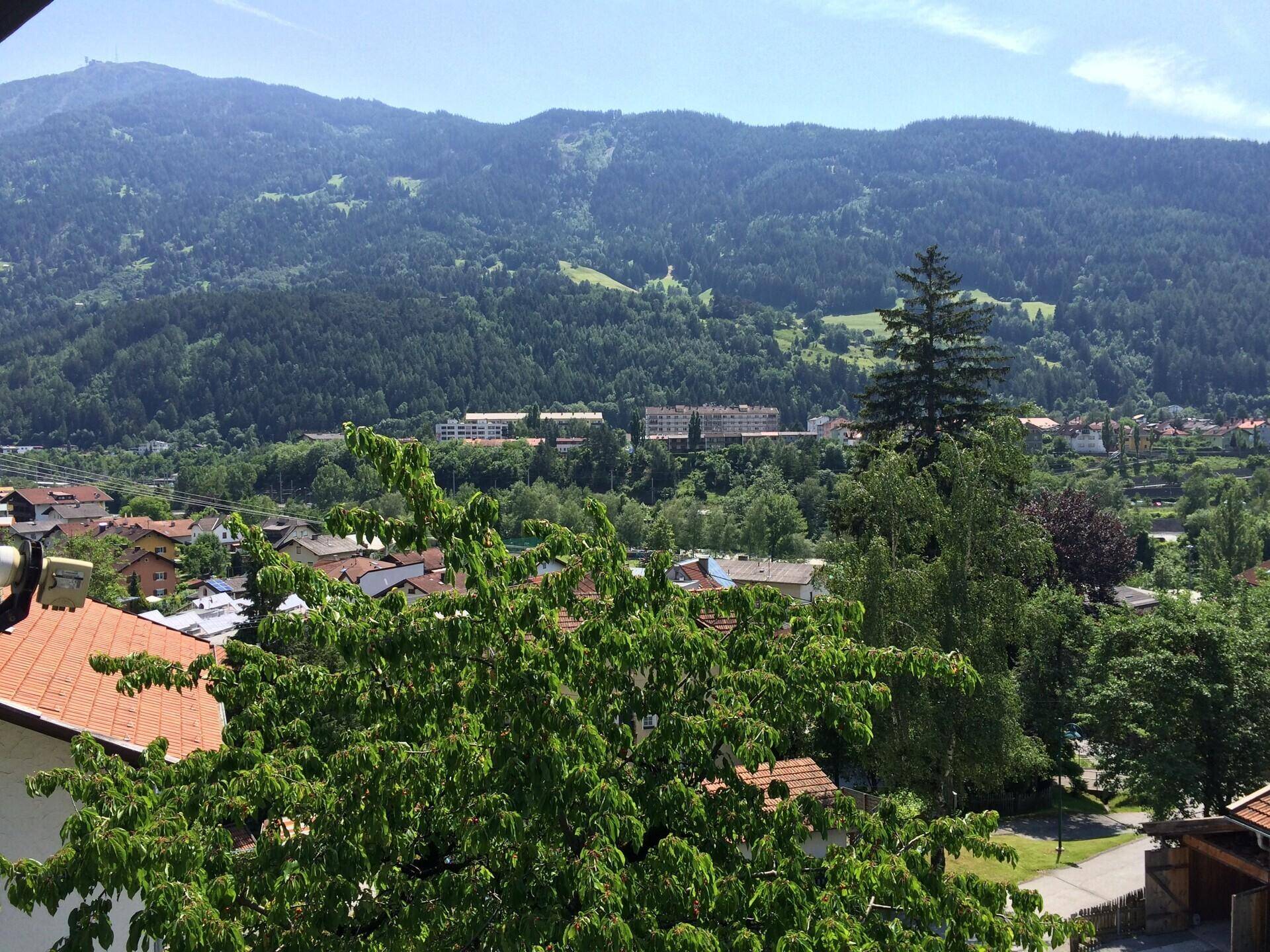 Weitblick über eine grüne Tallandschaft mit Siedlung und bewaldeten Bergen unter blauem Himmel.