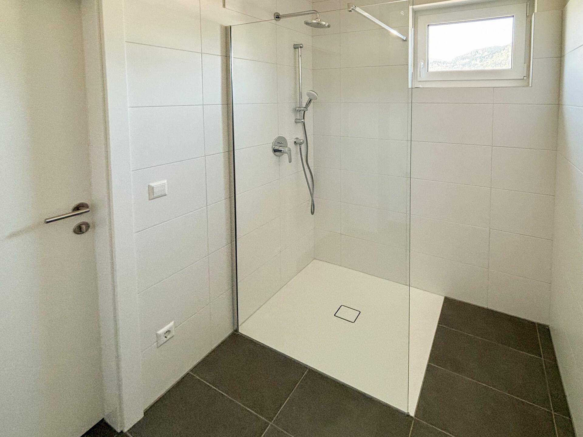 Modernes Badezimmer mit ebenerdiger Dusche, Glaswand und Fenster für Tageslicht.