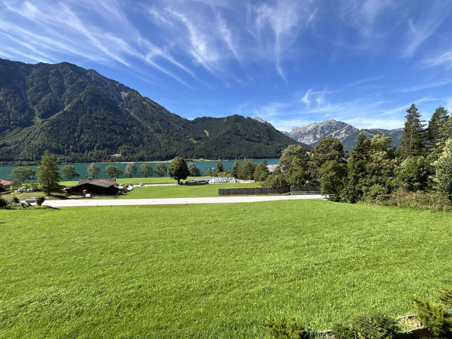 Weitläufige grüne Wiesen mit See- und Bergblick unter einem strahlend blauen Himmel.