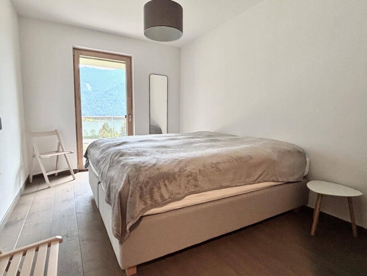 Schlafzimmer mit großem Bett, Holzboden und Zugang zu einem Balkon mit Bergblick.