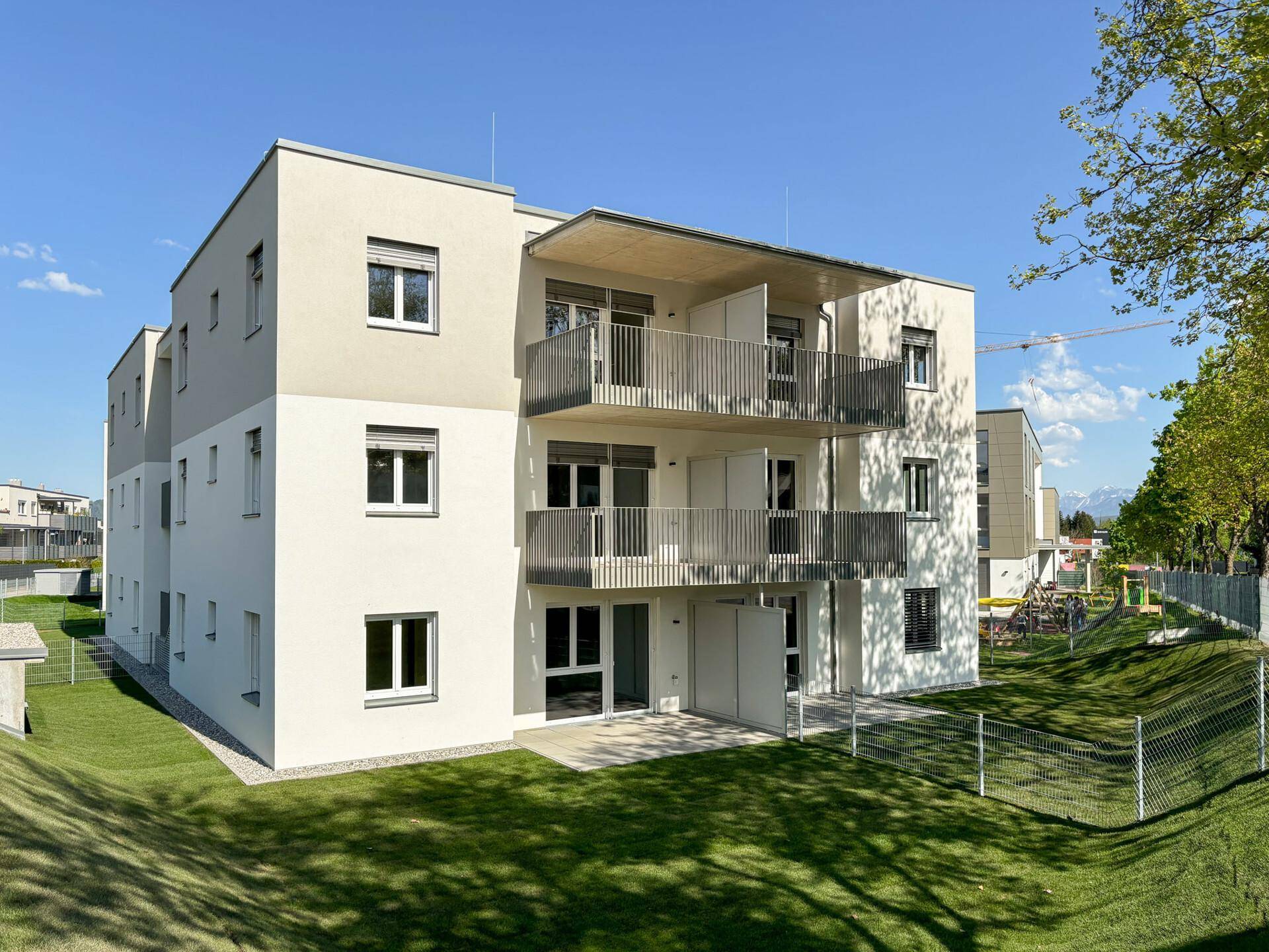 Modernes Mehrfamilienhaus mit gepflegter Rasenfläche und Spielplatz in sonniger Lage.
