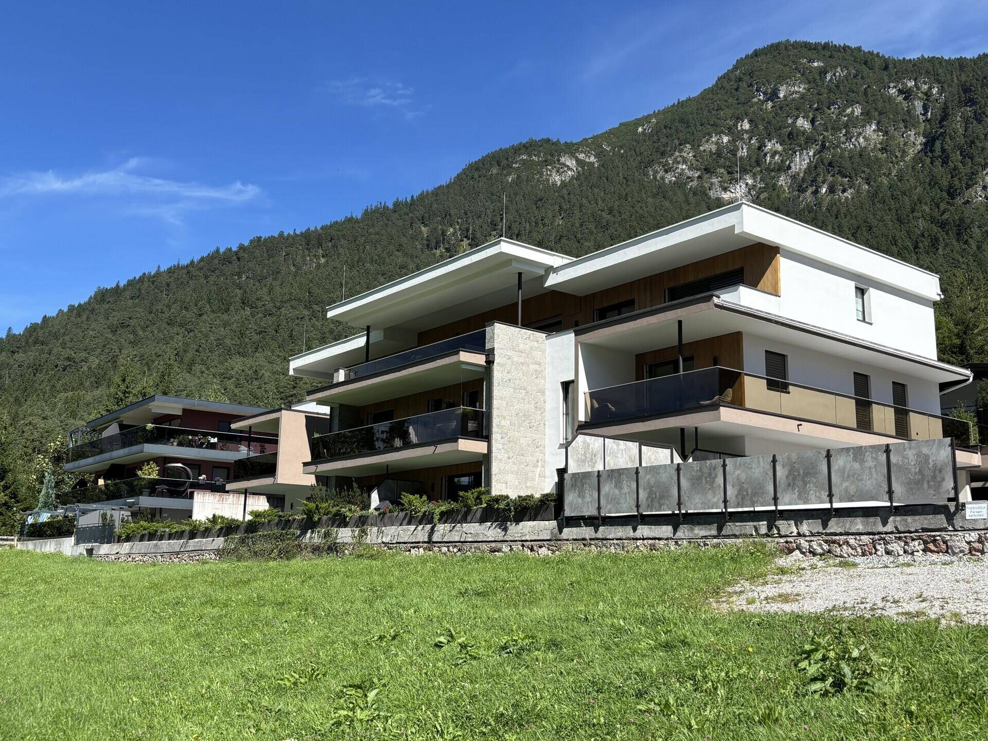 Moderne Architektur des Gebäudes mit mehreren Balkonen und einer beeindruckenden Bergkulisse im Hintergrund.
