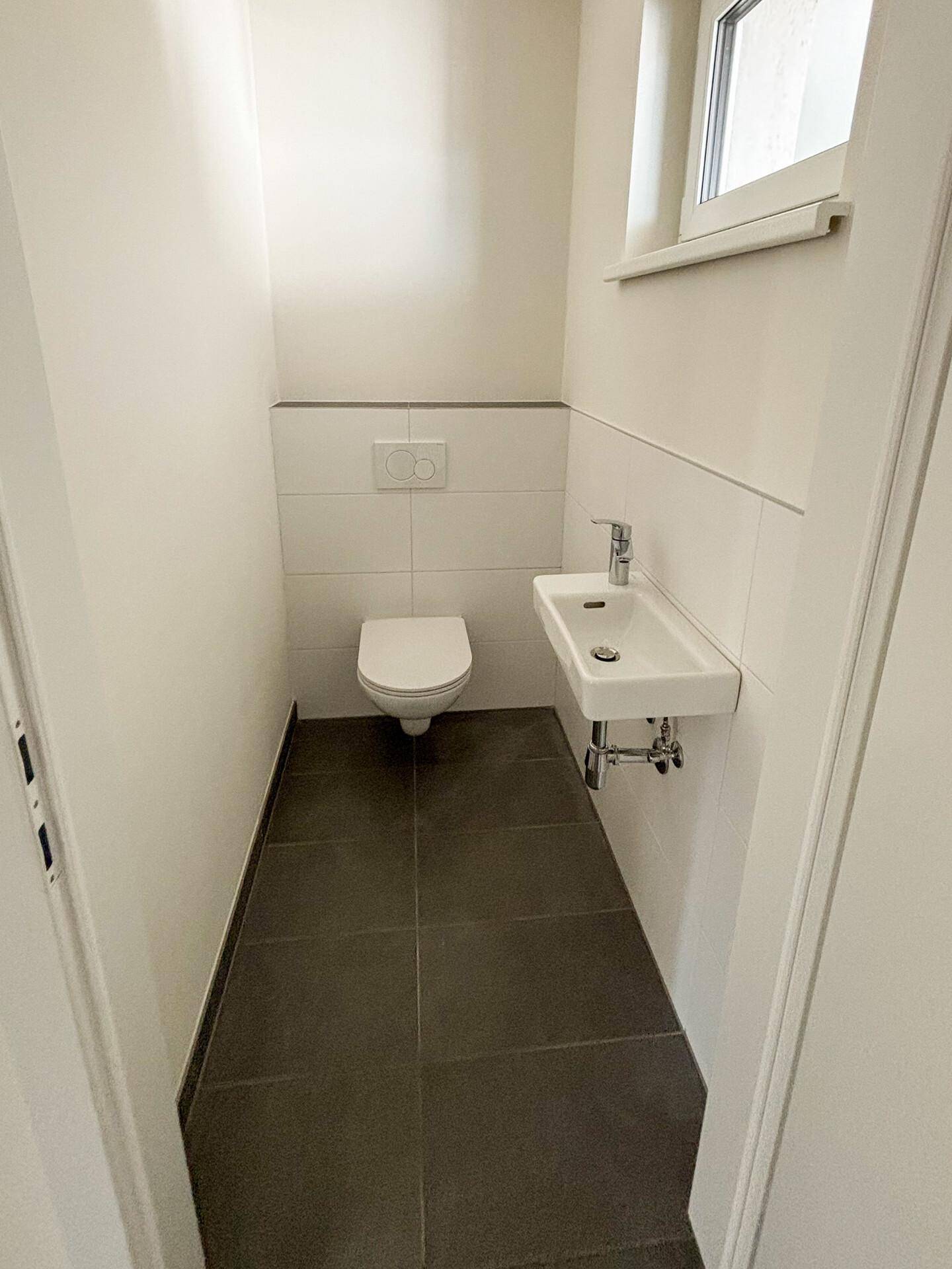 Separates Gäste-WC mit wandhängender Toilette und kleinem Waschbecken.