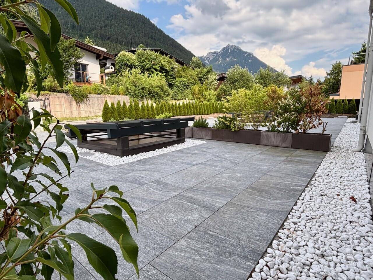 Großzügige Terrasse mit modernen Pflanzkübeln und einem Lounge-Bereich, umgeben von Natur.