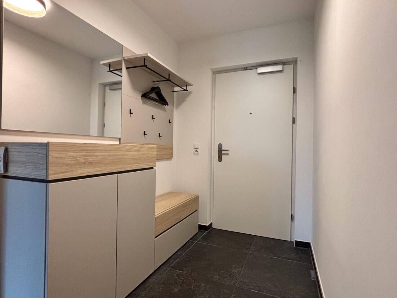 Heller Eingangsbereich mit Garderobe, Spiegel und dunklen Fliesen, bietet praktischen Stauraum.