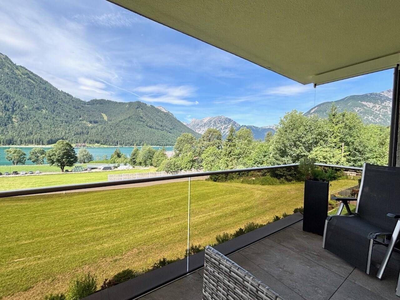 Sonniger Balkon mit Glasbrüstung und freiem Blick auf den Achensee und die majestätischen Berge.