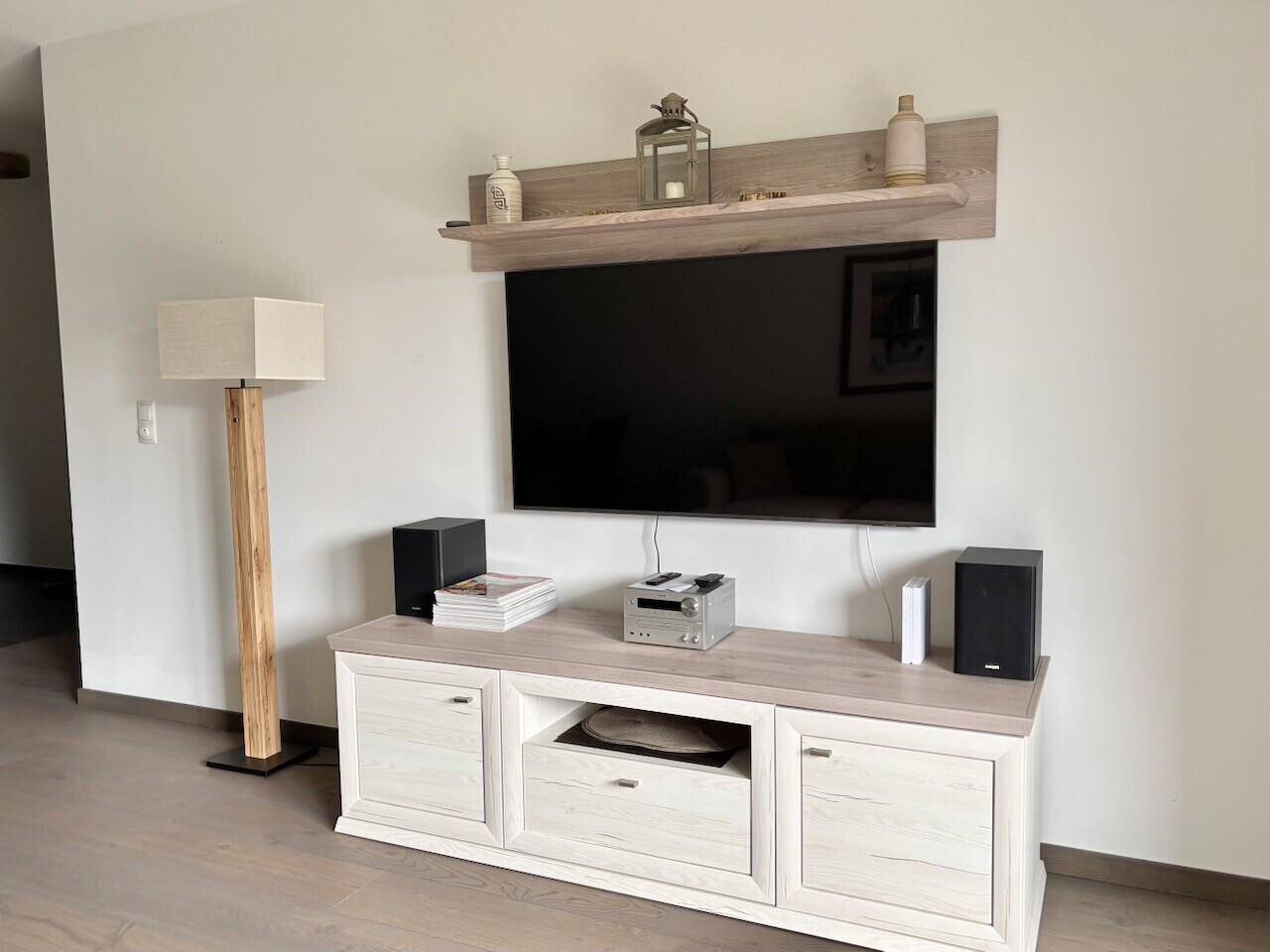 Wohnbereich mit großem Flachbildfernseher, elegantem Sideboard und Stehlampe.