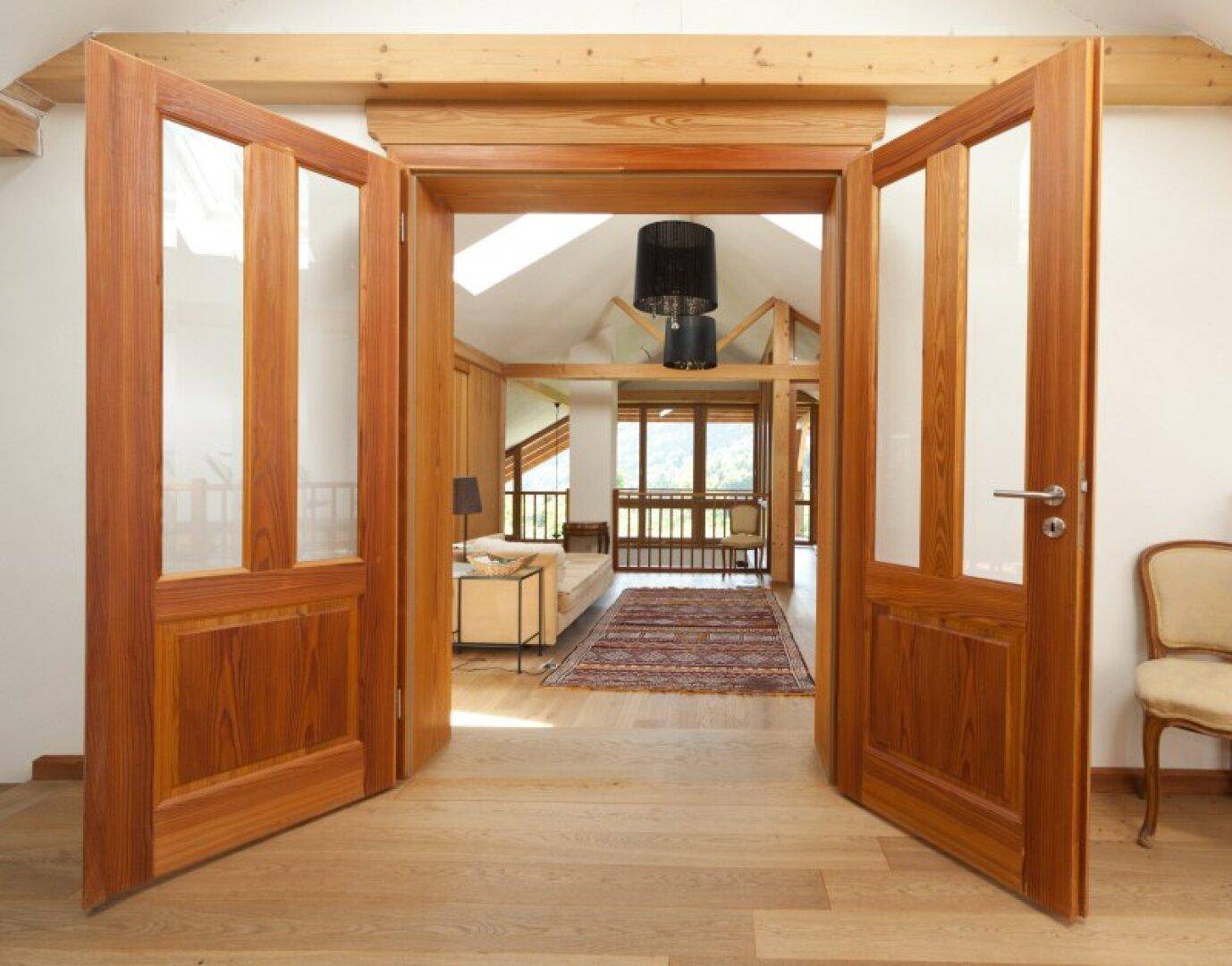 Offene Holztüren führen in einen hellen Wohnbereich mit Holzbalken und Parkettboden.