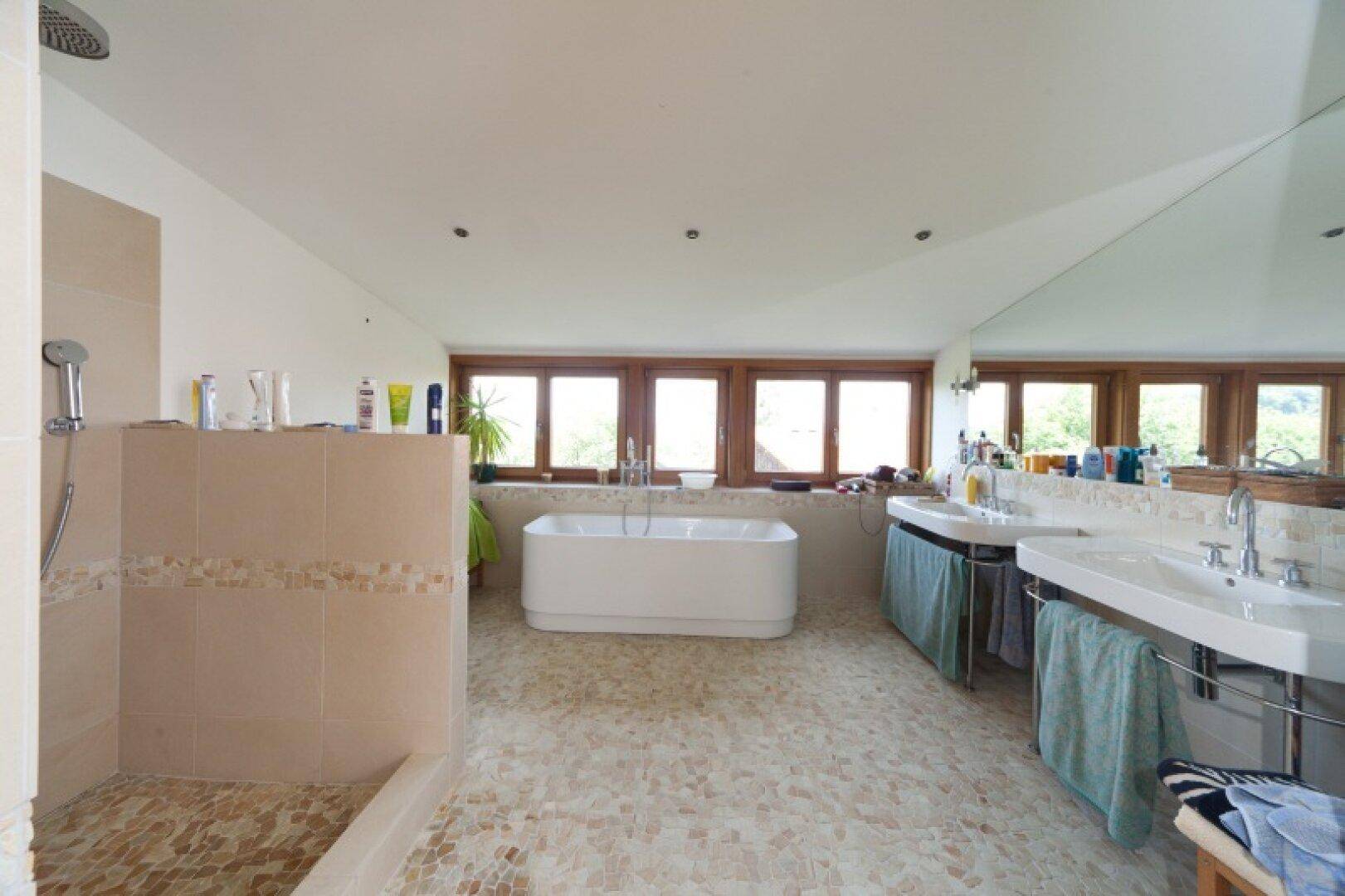 Geräumiges Badezimmer mit freistehender Badewanne, Doppelwaschbecken und Fensterfront.