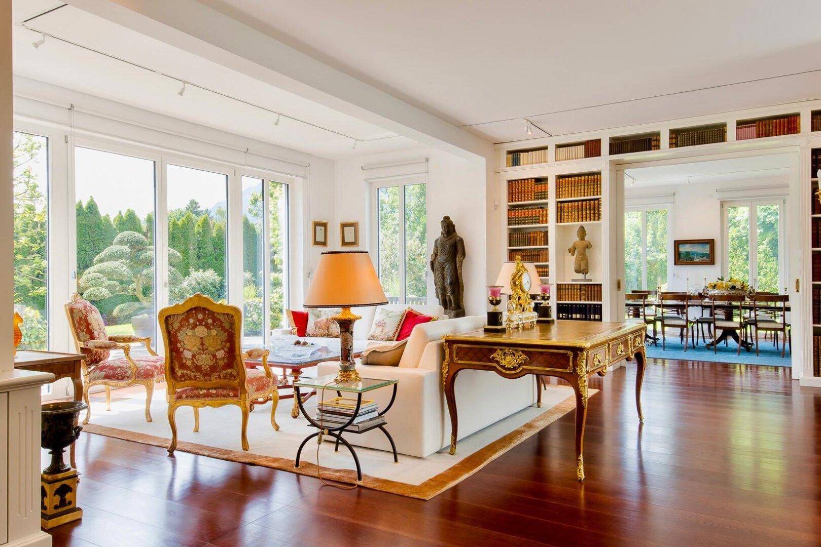 Helles Wohnzimmer mit großen Fenstern, Blick in den Garten und luxuriöser klassischer Einrichtung.