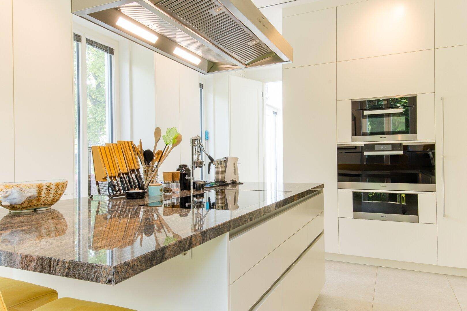 Moderne Küche mit weißer Front, großer Kücheninsel und hochwertigen Miele-Einbaugeräten.