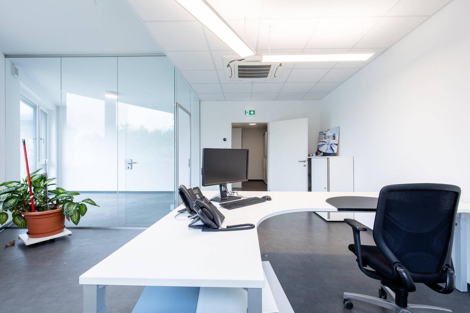 Funktionales Büro mit modernem Schreibtisch, Bürostuhl und einer eleganten Glaswand für offene Raumgestaltung.