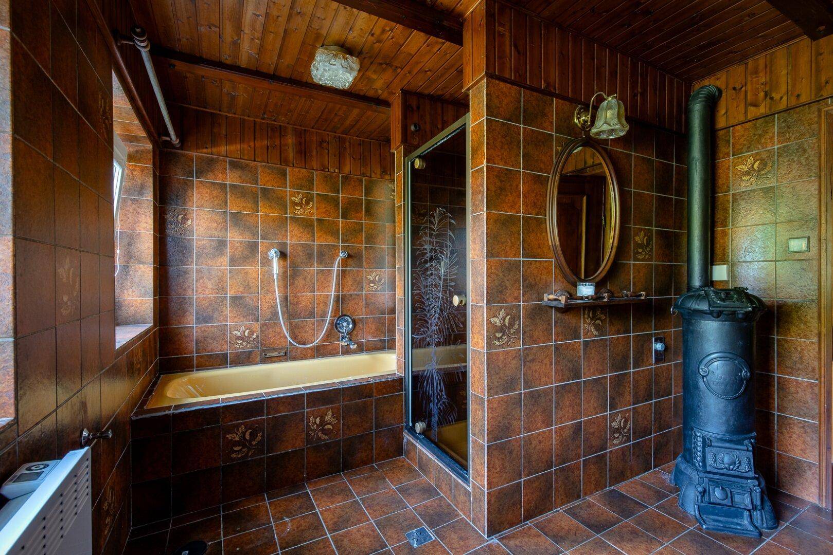 Rustikales Badezimmer mit braunen Fliesen, einer Badewanne, Dusche und einem traditionellen Ofen.