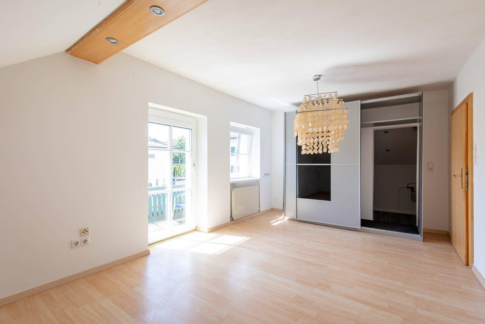 Helles Schlafzimmer mit hellem Laminatboden, Zugang zu einem Balkon und einem großen Kleiderschrank.
