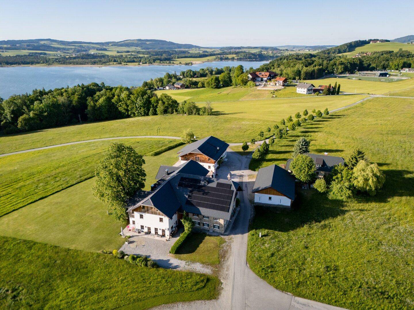 Luftaufnahme eines weitläufigen Anwesens mit mehreren Gebäuden, See und grüner Landschaft.