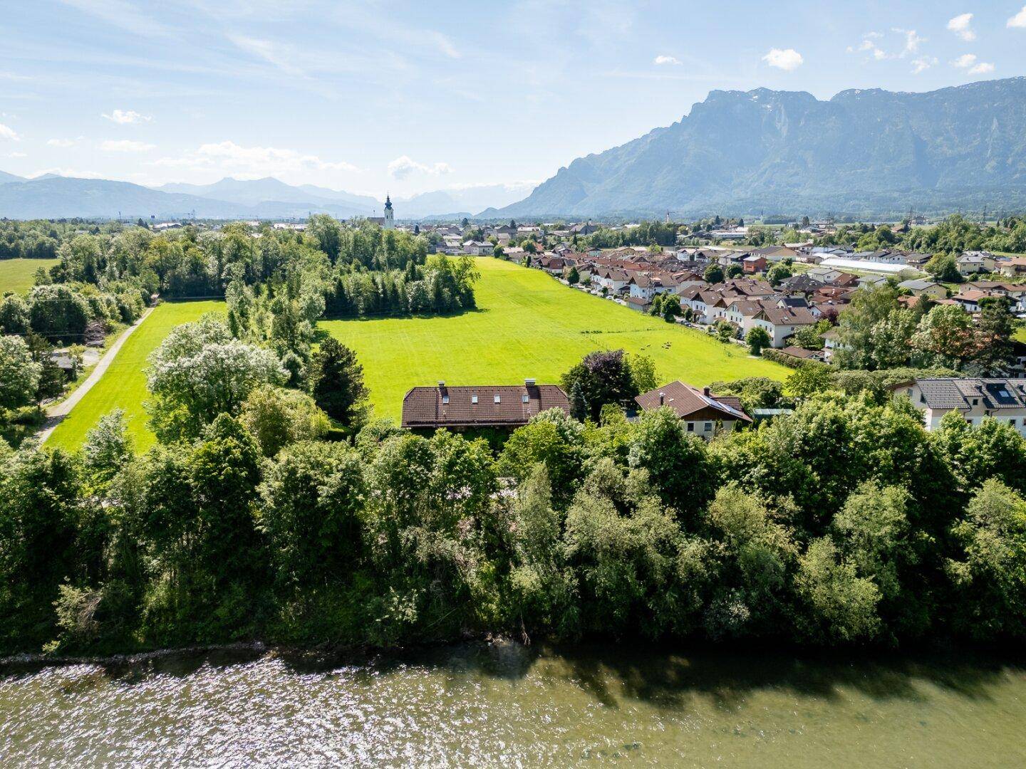 Weitläufiges Anwesen am Flussufer mit Blick auf Felder, Dorf und die majestätischen Berge.
