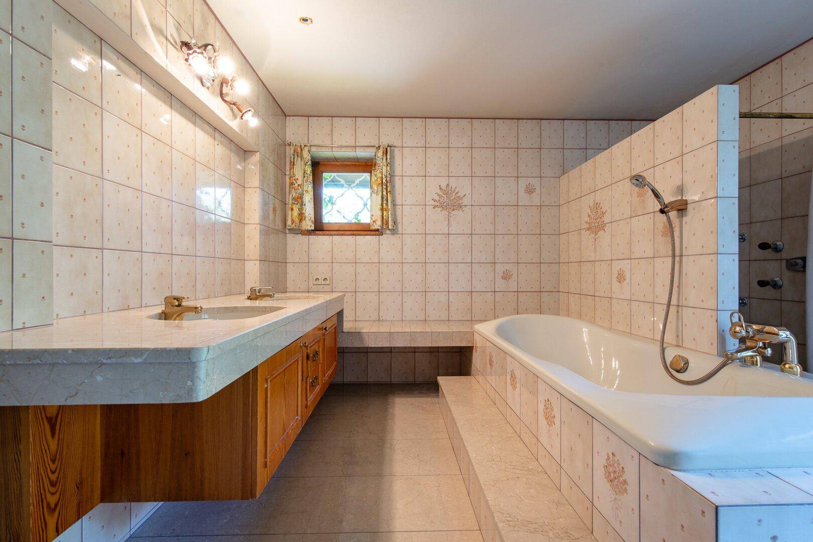Helles Badezimmer mit Doppelwaschbecken, Badewanne und traditionellen Fliesen an den Wänden.