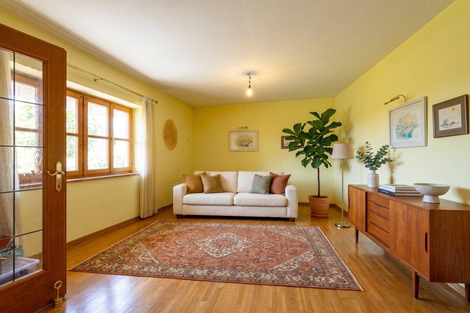 Freundliches Wohnzimmer mit gelben Wänden, Holzfußboden, bequemer Couch und orientalischem Teppich.