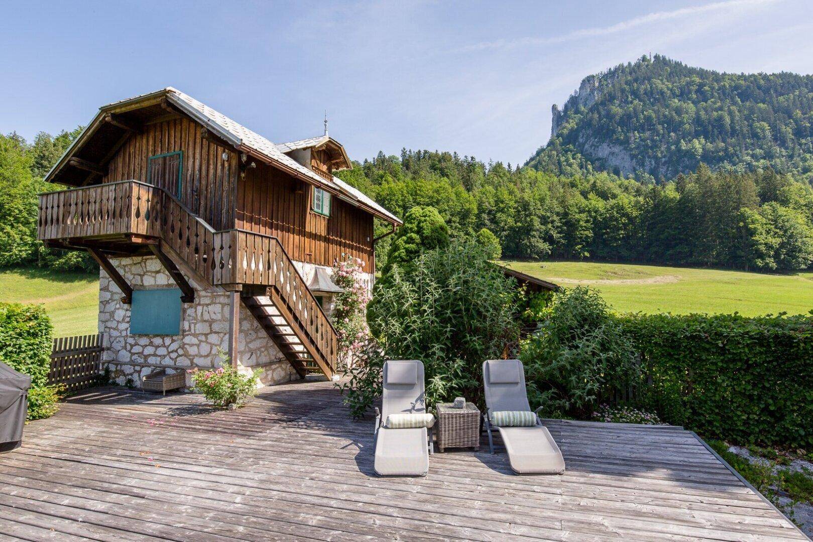 Geräumige Holzterrasse mit Liegestühlen und Blick auf die umliegende Berglandschaft.