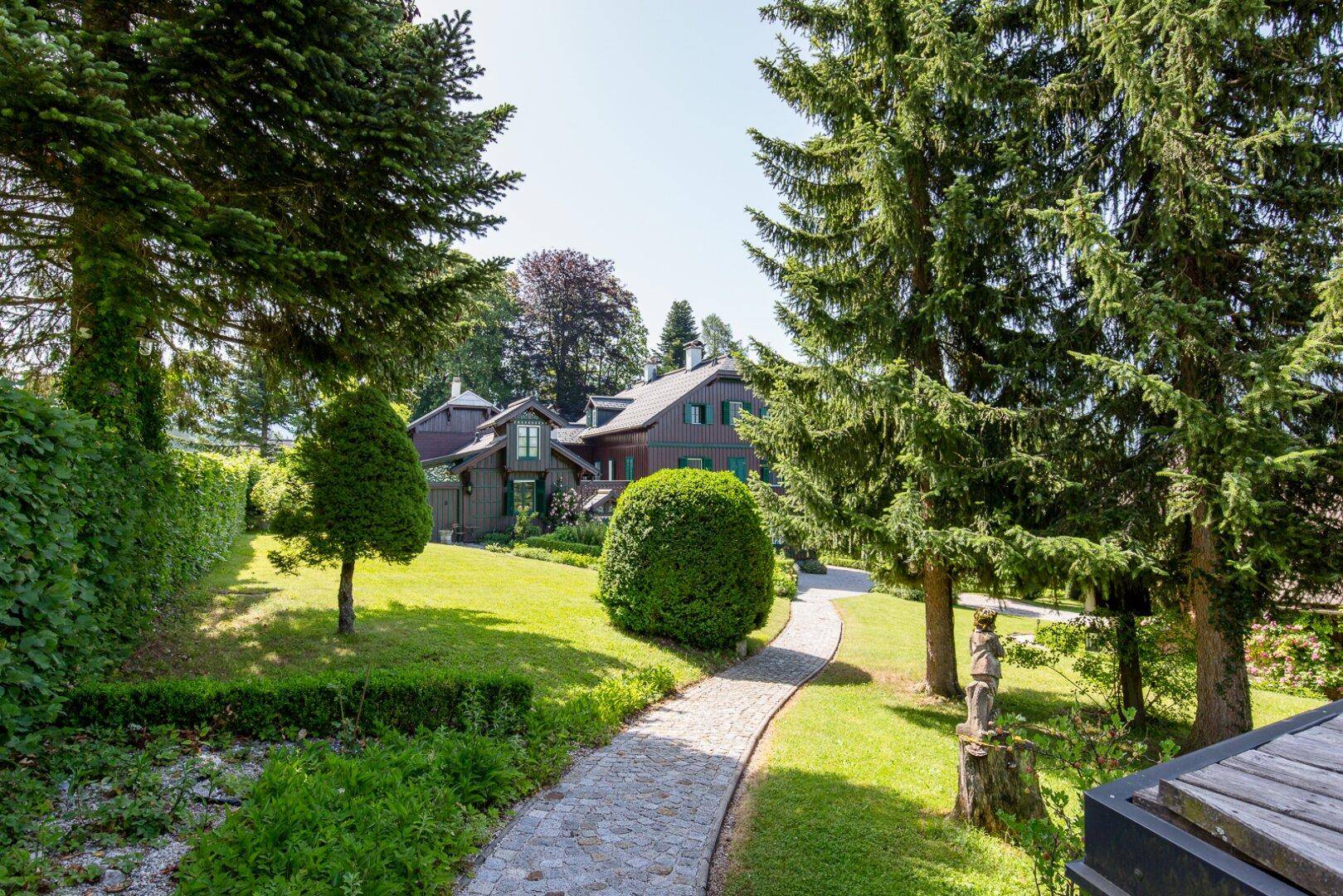 Idyllischer Gartenweg aus Kopfsteinpflaster, umgeben von gepflegten Hecken und hohen Bäumen.