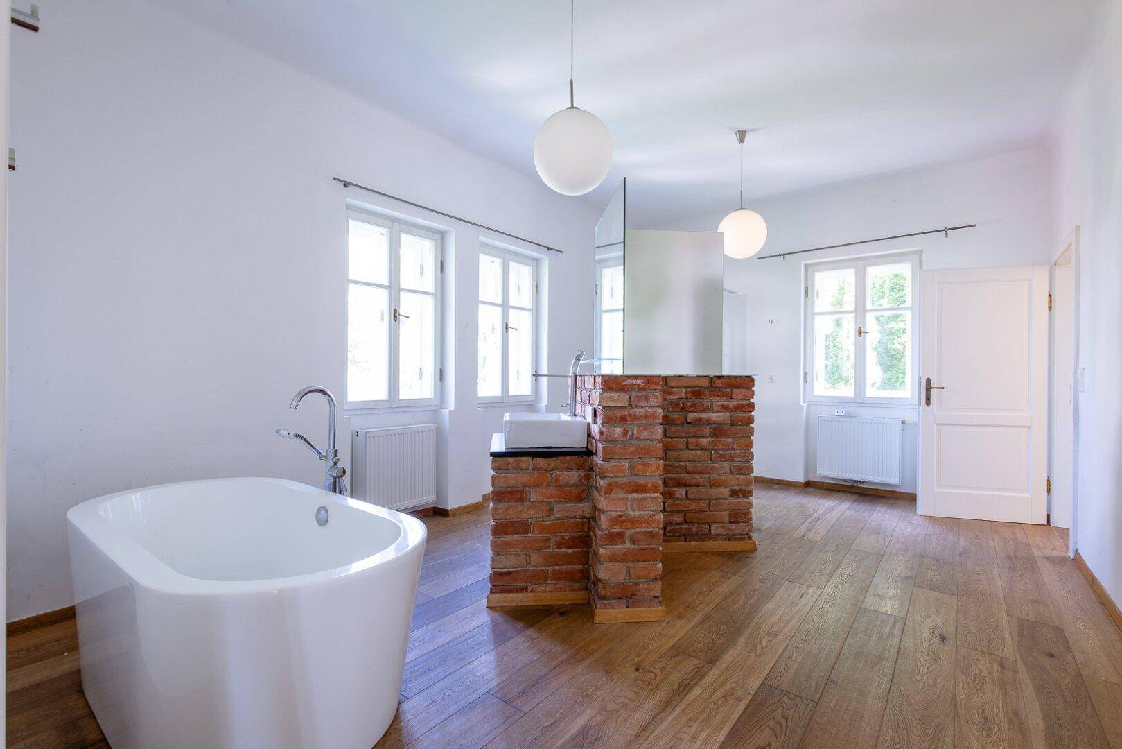 Modernes Badezimmer mit freistehender Badewanne, Holzboden und Ziegelwand-Akzent.