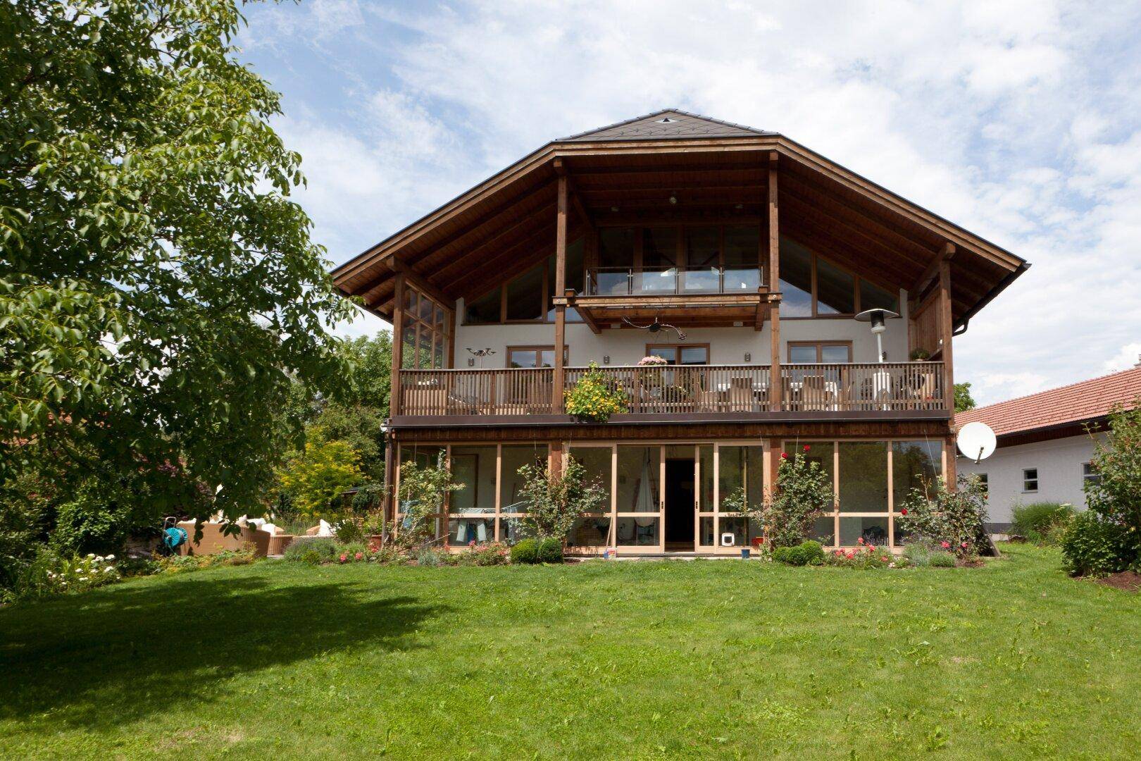 Großzügiges Holzhaus mit mehreren Balkonen und großen Fensterfronten in ländlicher Umgebung.