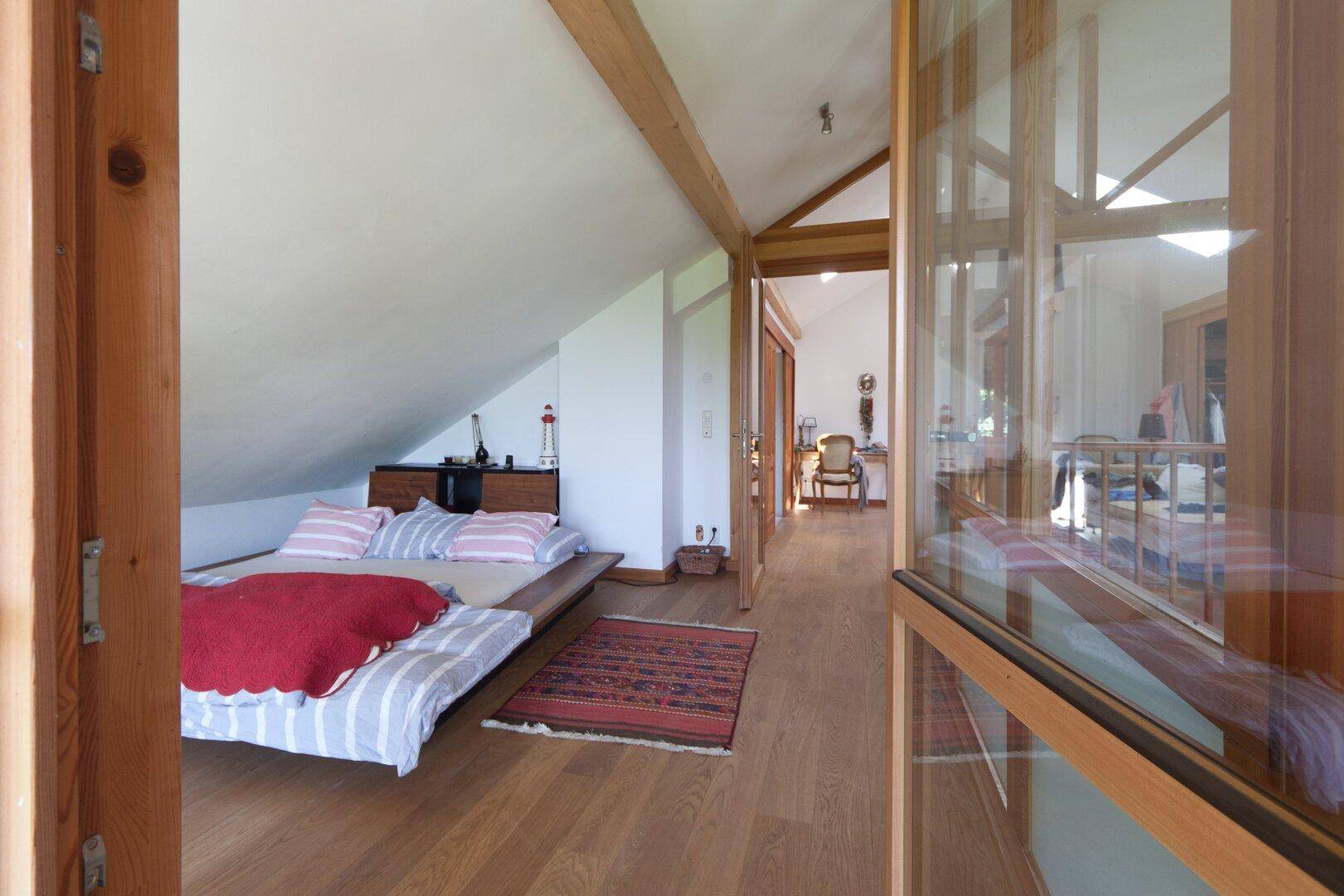 Helles Schlafzimmer im Dachgeschoss mit Holzboden, Dachschräge und Blick in den Wohnbereich.