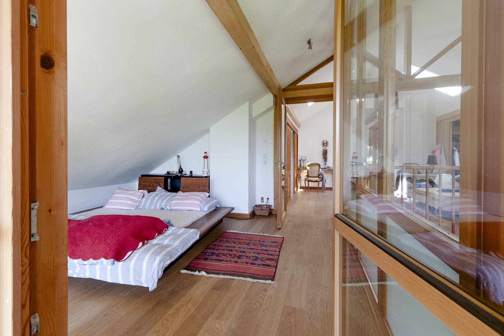 Gemütliches Schlafzimmer im Dachgeschoss mit Holzbalken und Holzboden.
