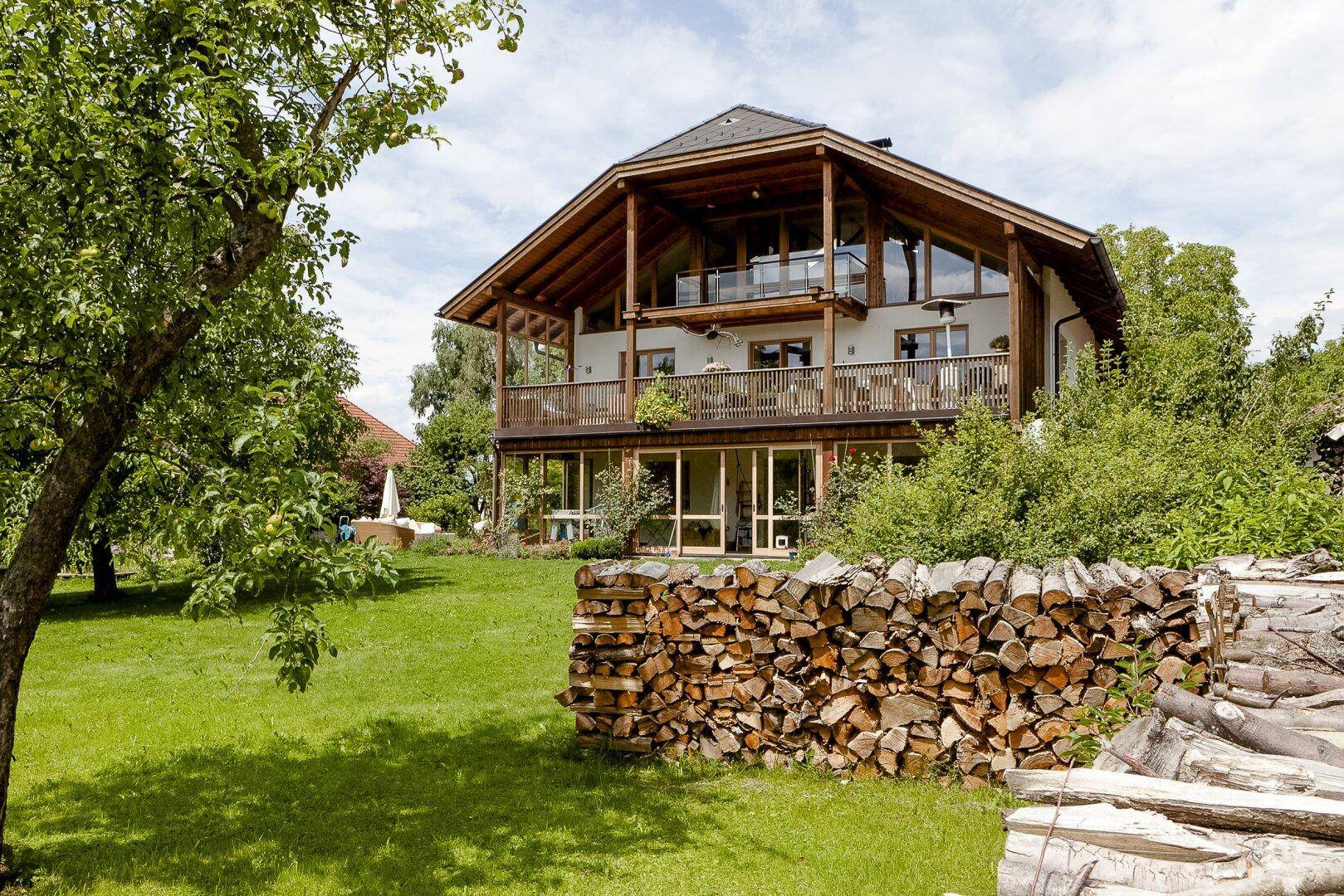 Großes Haus mit Holzfassade, Balkonen und weitläufigem Garten mit Holzstapel.