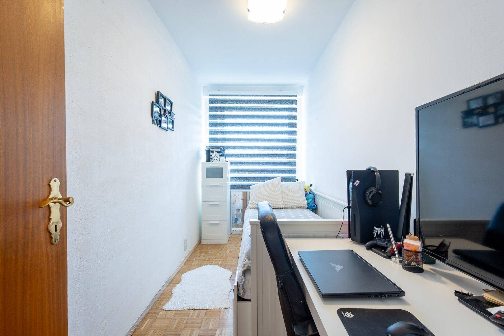 Kleines Zimmer, eingerichtet als Büro mit Schreibtisch, Computer und Einzelbett.