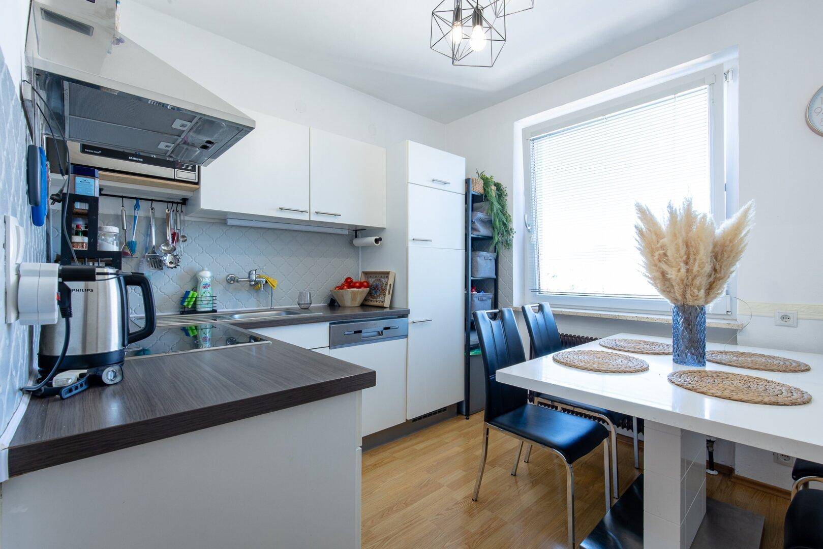 Moderne Küche mit weißen Schränken, dunkler Arbeitsplatte und Essbereich am Fenster.