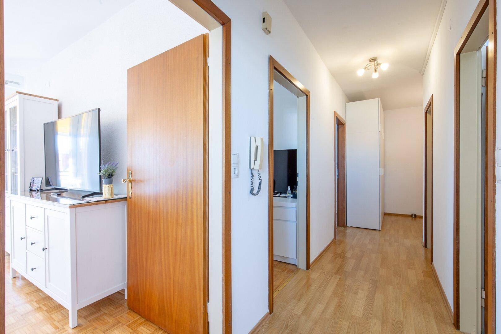 Heller Flur mit Holzparkettboden, weißen Wänden und mehreren Türen zu den Zimmern.