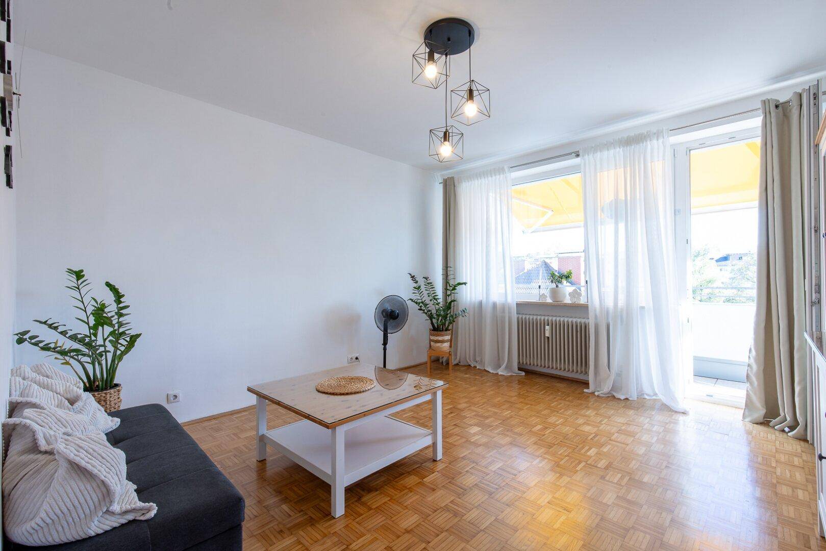 Gemütliches Wohnzimmer mit Parkettboden, Sofa, Couchtisch und Zugang zum Balkon.