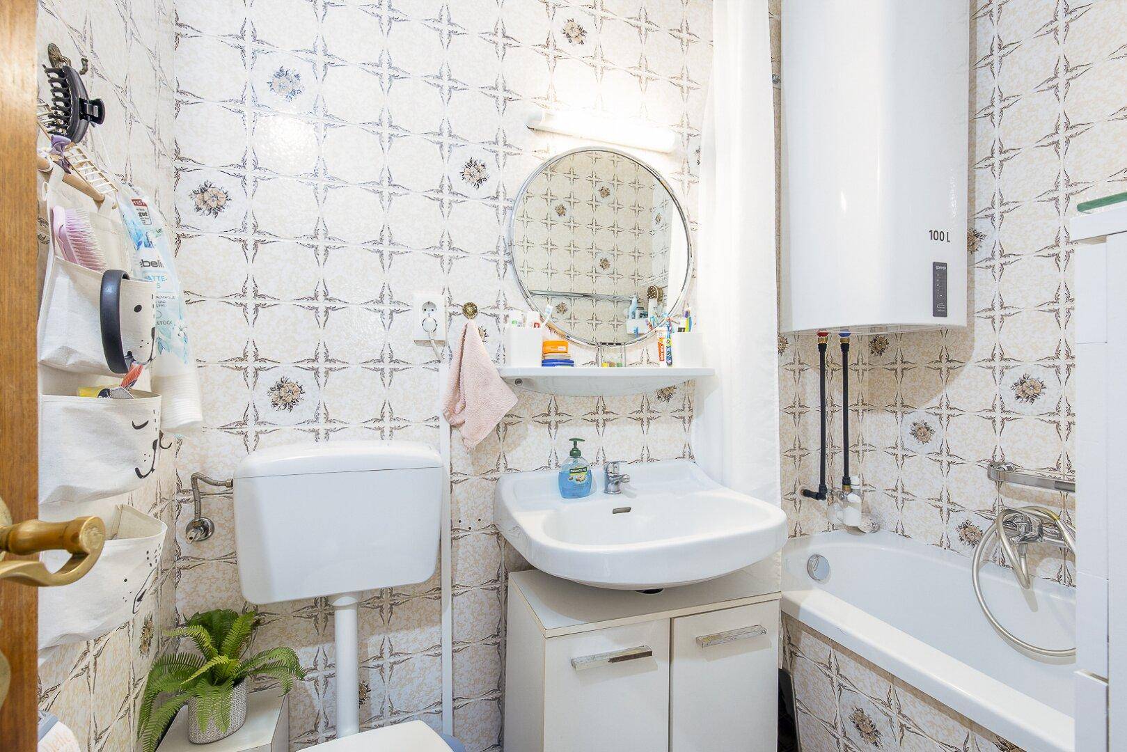 Funktionales Badezimmer mit gemusterten Fliesen, Badewanne, WC und Waschbecken mit Spiegelschrank.