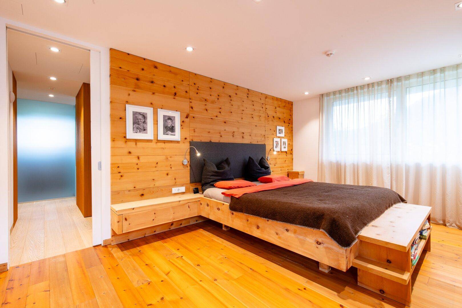 Gemütliches Schlafzimmer mit Holzwandverkleidung, Holzbett und hellem Parkettboden.