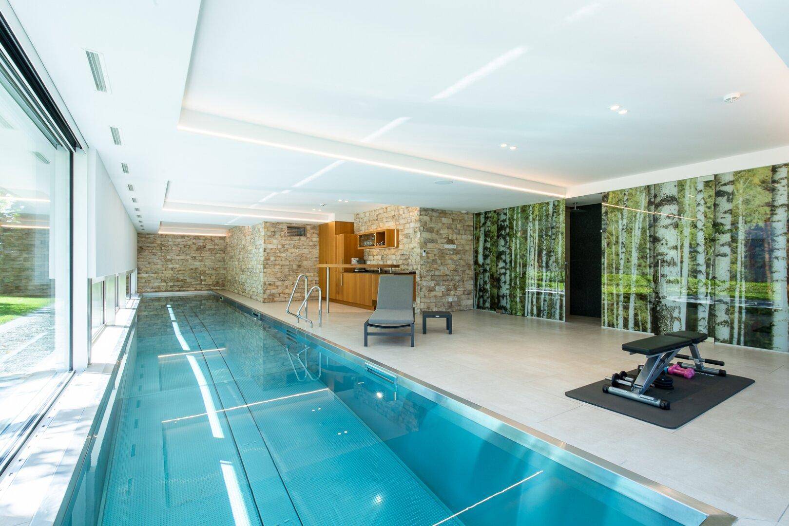 Exklusiver Wellnessbereich mit langem Innenpool, Fitnessgeräten und Steinwand-Akzenten.