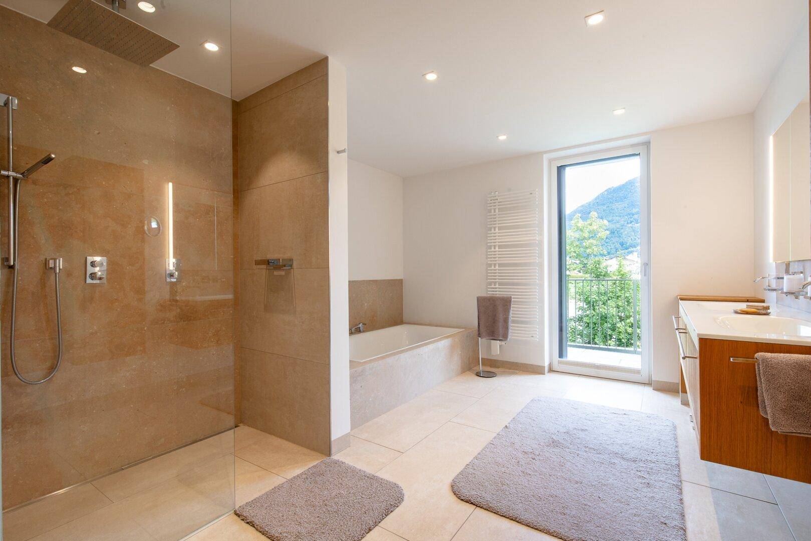 Modernes Badezimmer mit großer begehbarer Dusche, Badewanne und Zugang zum Balkon mit Bergblick.