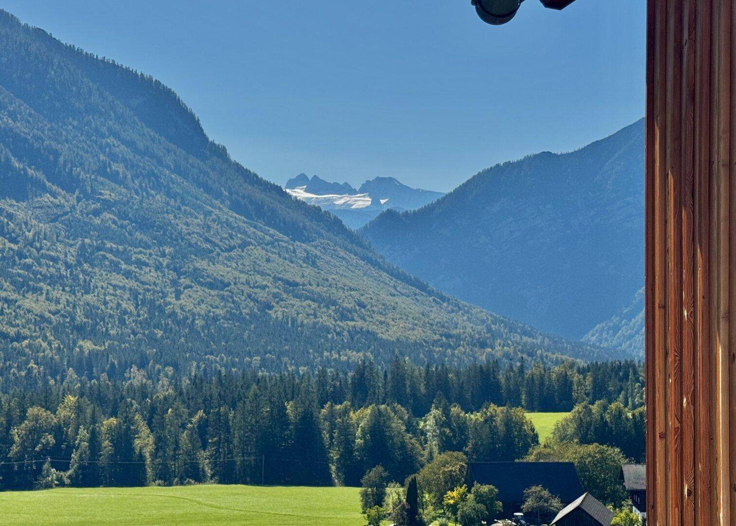 Malerischer Blick auf die weite Berglandschaft mit grünen Wäldern und einem schneebedeckten Gipfel.