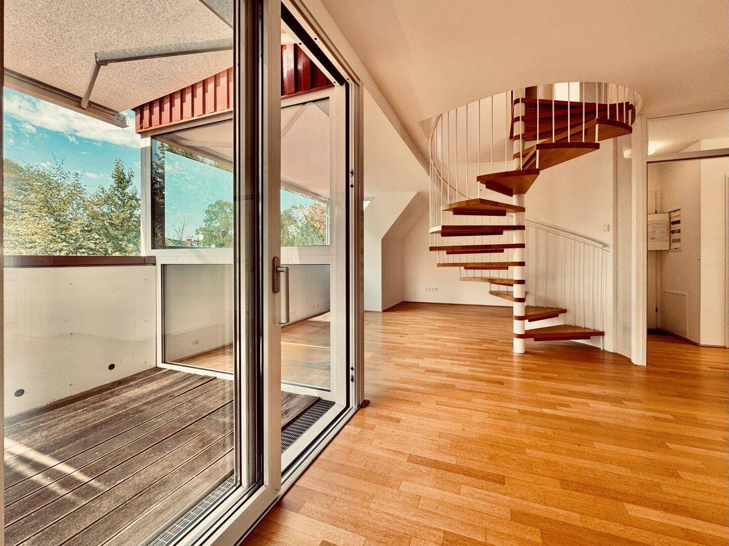 Lichtdurchfluteter Raum mit Holzfußboden, Wendeltreppe und großem Balkonzugang.