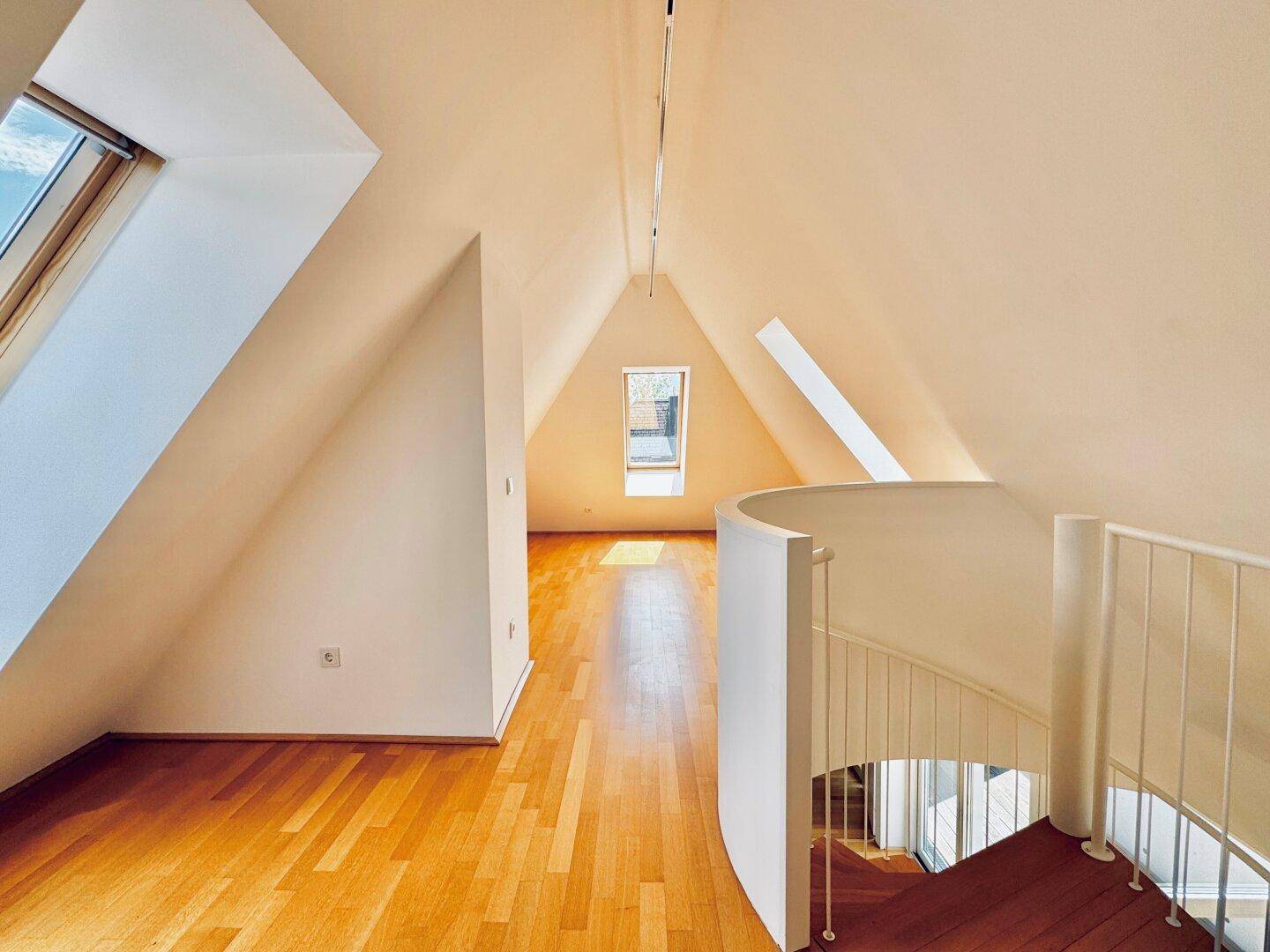 Geräumiger Dachboden mit Holzboden, schrägen Wänden und Dachfenstern für viel Licht.