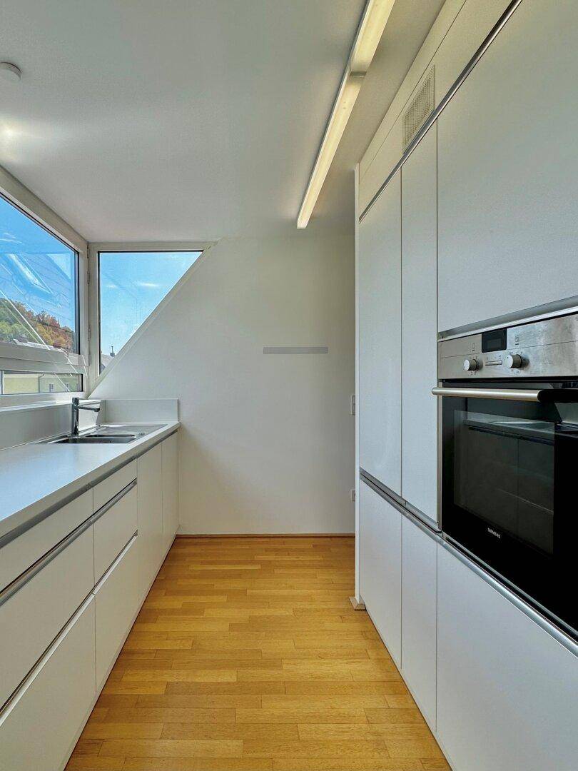 Helle Einbauküche mit weißen Fronten, integriertem Backofen und Holzfußboden.