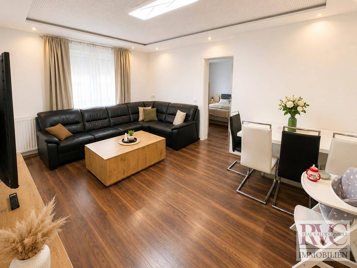 Geräumiger Wohn-Essbereich mit dunklem Laminatboden, Ledersofa und Esstisch.