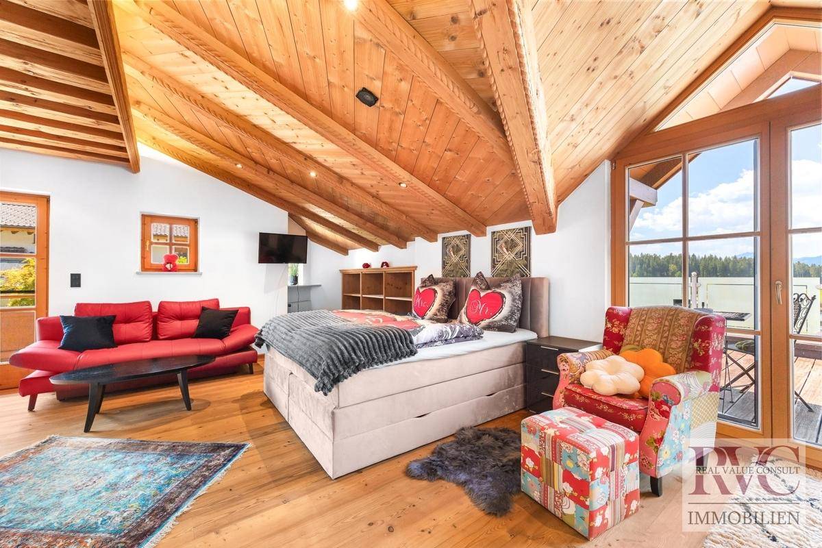 Großes Schlafzimmer im Dachgeschoss mit Holzbalkendecke, rotem Sofa und weitem Ausblick.