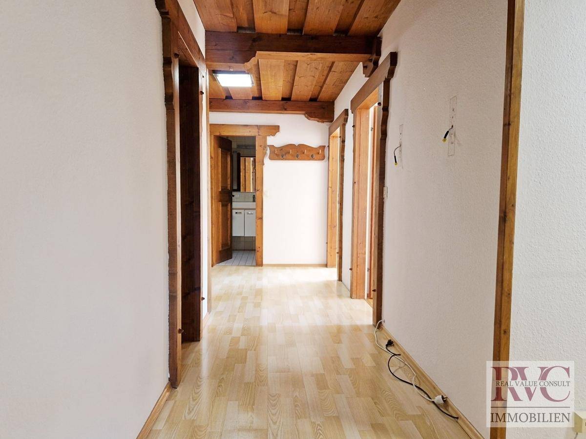 Langer Flur mit Laminatboden und Holzbalkendecke, führt zu weiteren Räumen.