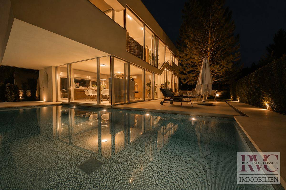 Beleuchteter Poolbereich bei Nacht mit moderner Architektur und großen Glasfronten.