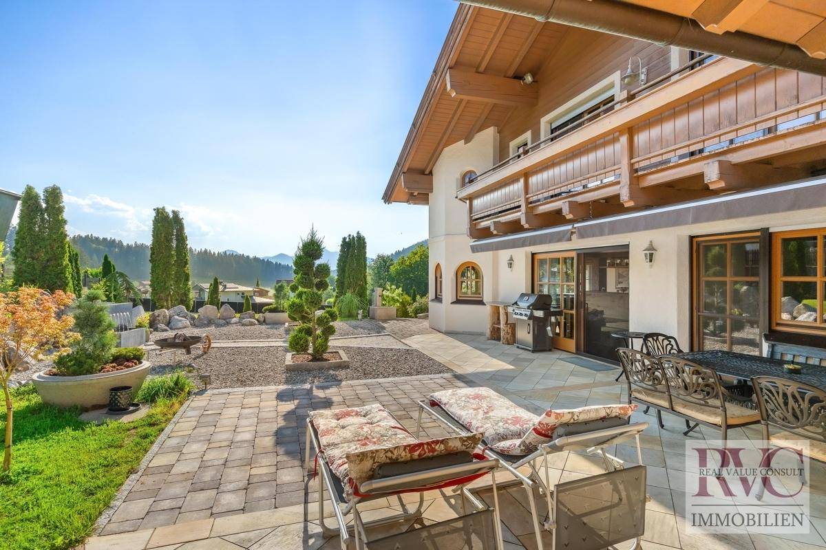 Große gepflasterte Terrasse mit Gartenmöbeln, Grillbereich und Blick auf den gepflegten Garten.